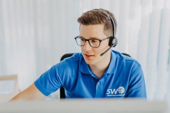 Auszubildender telefoniert mit einem Headset vor einem Computer.